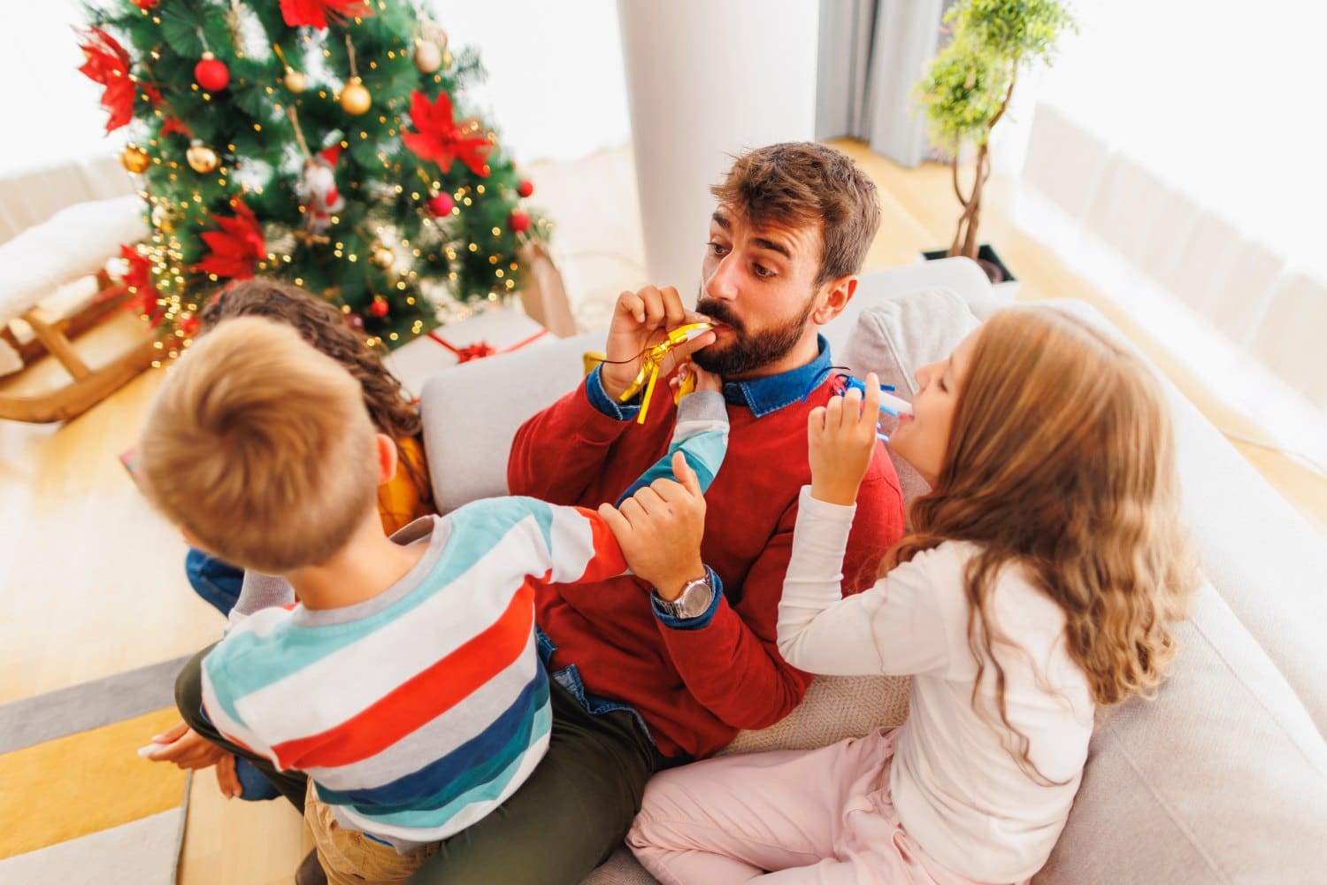 Parents having fun playing with children while spending Christmas at home, blowing party whistles and laughing