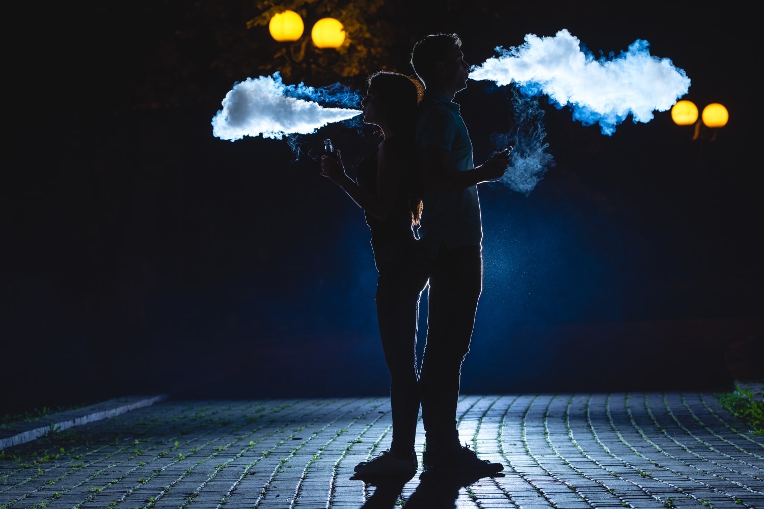 The couple smoke an electric cigarette on the dark alley. night time
